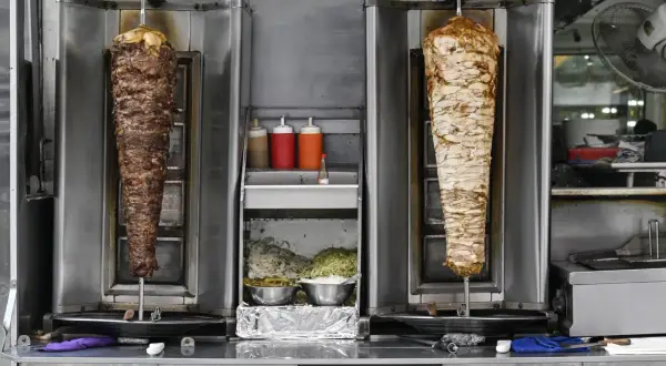 Dwa pionowe rożna z mięsem do kebaba, jeden z wołowiny, drugi z kurczaka. Obok sosy i surówki. Zastanawiasz się, ile kosztuje mały kebab?