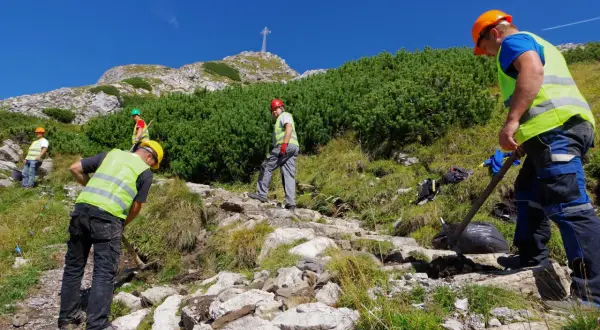 Pracownicy konserwują szlak na Giewont. Czy szlak na Giewont jest trudny? Widać krzyż na szczycie, a teren jest kamienisty.