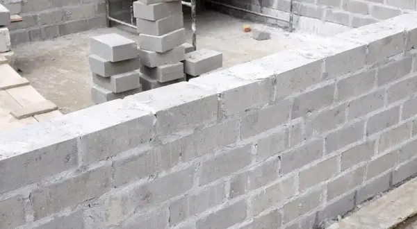 Budowa fundamentów z bloczków betonowych. Stos świeżo ułożonych bloczków betonowych fundamentowych obok wznoszonej ściany.
