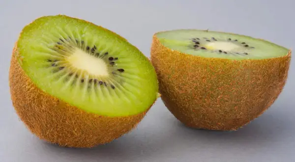 Dwa połówki kiwi na szarym tle. Zastanawiasz się, ile kalorii ma kiwi? To niskokaloryczny owoc, idealny na zdrową przekąskę.