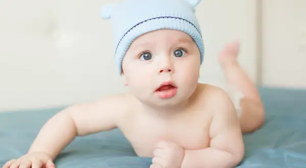 Adorable bébé garçon, prénom S, porte un bonnet bleu avec des oreilles. Il est couché sur le ventre, les yeux grands ouverts.