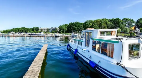 Ein Hausboot liegt im Hafen an der Mecklenburgischen Seenplatte. Ein Holzsteg führt ins klare Wasser.