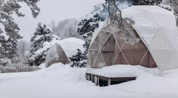 Śnieżne krajobrazy i przytulne domki do wynajęcia na weekend. Dym unosi się z komina jednego z igloo, zapraszając do środka.