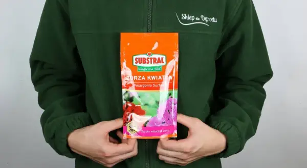 Opakowanie nawozu Substral Burza Kwiatów z pelargoniami, trzymane przez osobę w zielonej bluzie.