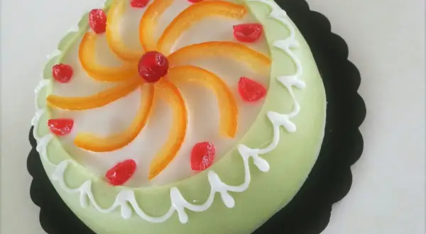 Gâteau sicilien vert pâle glacé, décoré de zestes d'orange, de fruits confits rouges et de glaçage blanc.