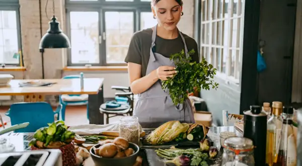 Frau bereitet frisches Gemüse für eine gesunde Ernährung zu. Kräuter, Mais und Pilze auf dem Tisch, inspiriert von der planetary health diet.