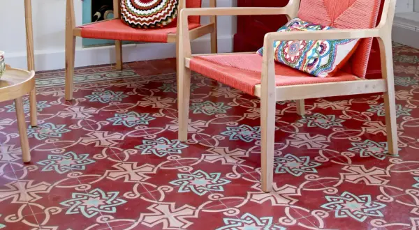 Sol rouge orné de motifs géométriques complexes, typiques des pose carreaux de ciment. Deux fauteuils orange vif avec coussins colorés.