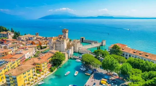 Garda città: castello Scaligero sull'acqua turchese, case colorate e barche ormeggiate.
