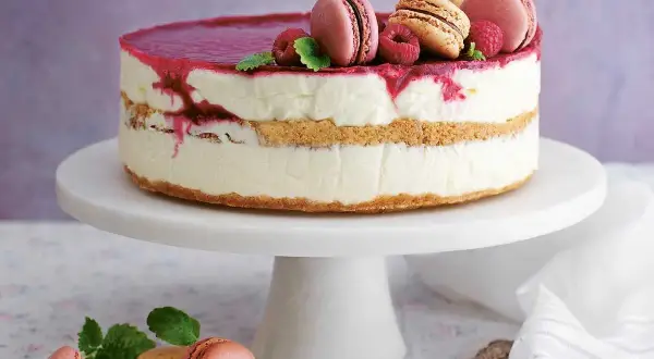 En vacker nyårstårta med lager av krämig fyllning, kexbotten och hallonspegel. Toppad med macarons, hallon och mynta. Ett perfekt nyårstårta recept!