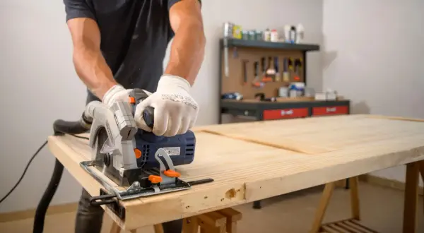 Hombre con guantes usa sierra circular para cortar una puerta de madera. Aprende como enderezar una puerta de madera con esta técnica.