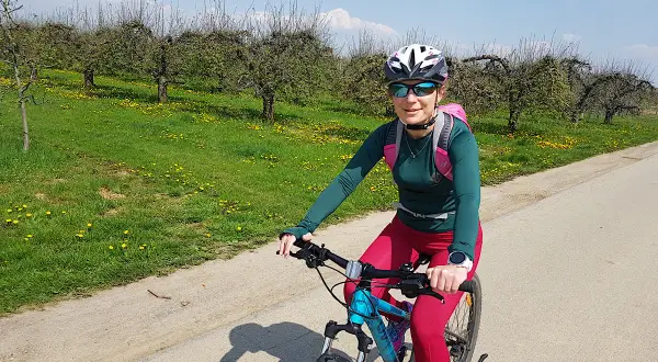 Kobieta na rowerze podziwia sandomierskie trasy rowerowe wśród kwitnących sadów.