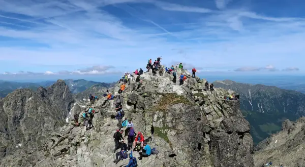 Tłum turystów na skalistym szczycie Rysów, być może 2499 czy 2503 m n.p.m. Podziwiają piękne widoki Tatr.