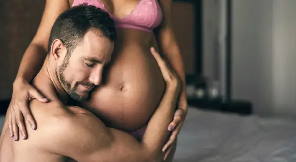 Czuły mężczyzna obejmuje brzuch ciężarnej kobiety. Delikatne pozycje seksualne w ciąży, pełne miłości i bliskości.