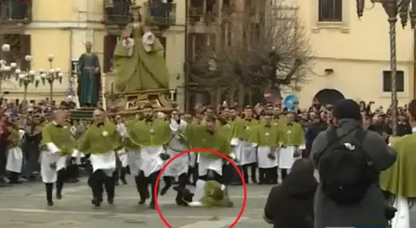 Durante una processione, un uomo cade a terra, quasi come una **madonna che scappa**, mentre altri partecipano con vesti verdi e bianche.