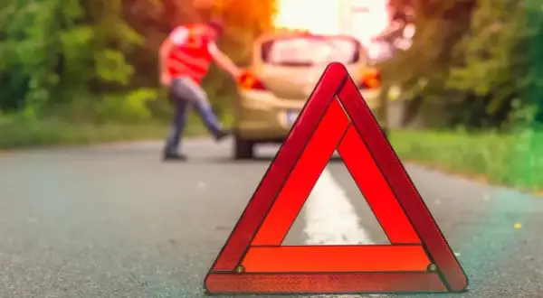 Trójkąt ostrzegawczy na drodze, gdzie nie można holować. Kierowca w kamizelce odblaskowej przy awaryjnym samochodzie.