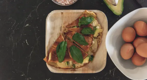 Pyszny omlet z awokado, podany na drewnianej tacce, z jajkami i solą himalajską w tle.