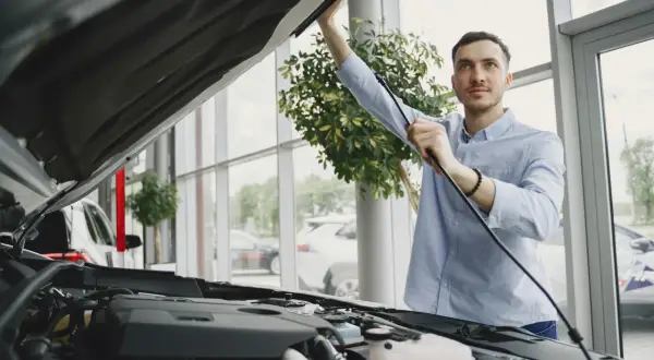 Un homme examine le moteur d'une voiture neuve dans un showroom. Il s'assure de la qualité avant de finaliser le prix de l'expertise voiture.