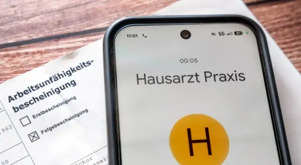 Arbeitsunfähigkeitsbescheinigung liegt bereit. Das Handy zeigt Anruf bei Hausarzt Praxis. Wichtig für Krankmeldung ab 3. Tag Gesetz.
