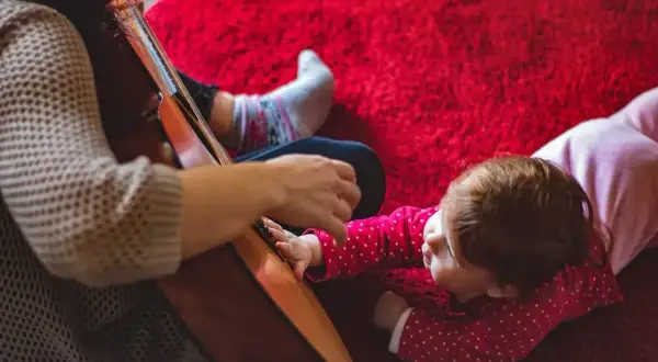 Dziecko słucha piosenek do prezentacji zdjęć z dzieciństwa, gdy ktoś gra na gitarze.