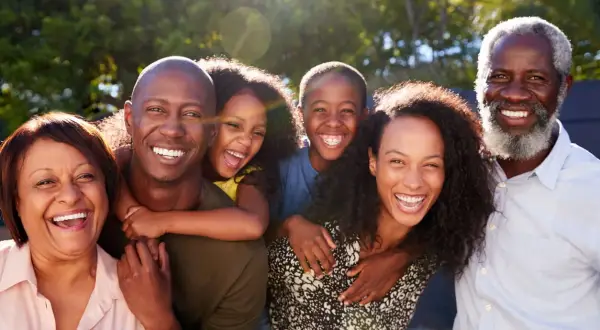 Una familia multigeneracional sonríe y ríe junta al aire libre, disfrutando de actividades de día familiar.