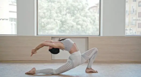 Mujer en postura de Anjaneyasana yoga, arqueando la espalda y extendiendo brazos hacia atrás.