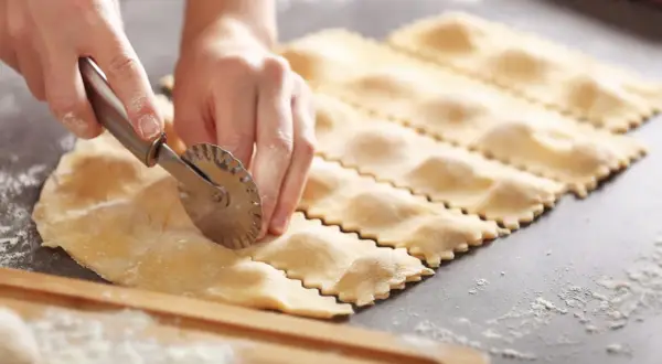 Hände schneiden mit einem Teigrädchen frische Ravioli. So einfach ist ravioli selber machen.