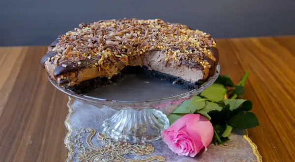 En läcker choklad cheesecake med chokladspån och nötter, serverad med en rosa ros.