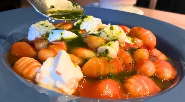 Pyszne makaron gnocchi z pomidorami, mozzarellą i zielonym sosem. Łyżka z sosem czeka na dodanie.