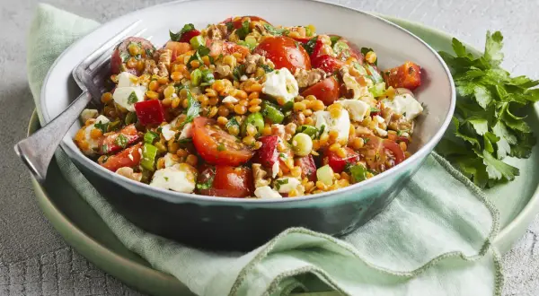 Ein bunter rote Linsen Salat mit Tomaten, Feta und Kräutern, appetitlich in einer Schüssel serviert.