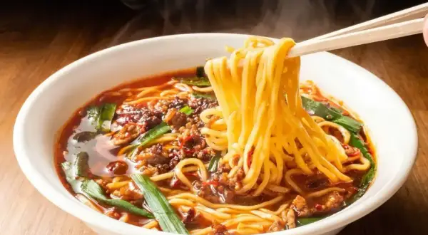 Gorący, parujący ramen z mięsem mielonym i szczypiorkiem. Pałeczki unoszą kłębek żółtego makaronu, zapowiadając, jak smakuje ramen.
