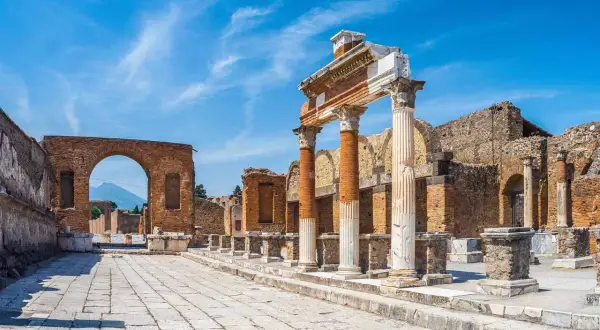 Ruines antiques de Pompéi sous un ciel bleu. Colonnes imposantes et un arc de brique invitent à visiter Pompéi et à imaginer la vie d'autrefois.