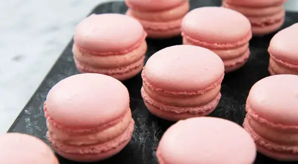 Rosa macarons på en mörk yta, perfekta för ett macarons recept.