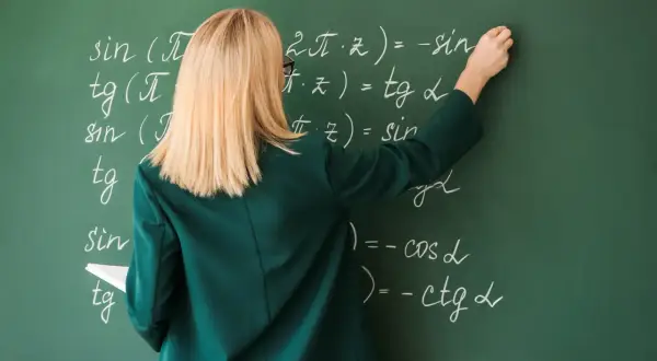 Nauczycielka pisze wzory matematyczne kredą na zielonej tablicy.