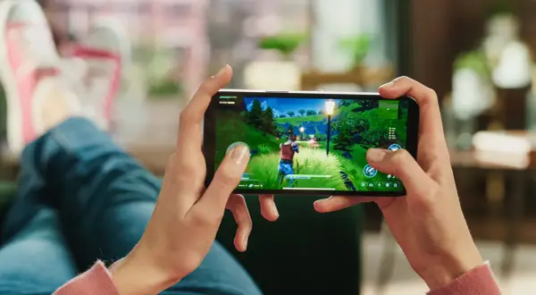 Dłonie trzymające smartfon z grą akcji w zielonym, bajkowym świecie.
