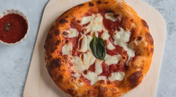 Pizza margherita appena sfornata, con crosta dorata e mozzarella filante. Accanto, una ciotolina di salsa di pomodoro, perfetta per chi ama la pizzelle ricetta tradizionale.
