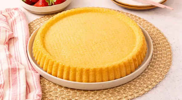 Ein goldbrauner, runder Kuchenboden, perfekt für ein Erdbeerboden Rezept. Daneben eine Schüssel mit frischen Erdbeeren.