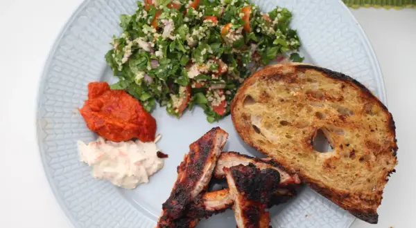 En tallrik med grillade revbensspjäll, rostat bröd, en krämig sallad och en fräsch tabbouleh. Perfekt för ett somrigt tabbouleh recept.