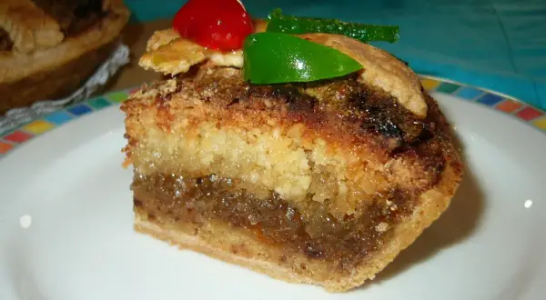 Rebanada de tarta de Mondoñedo, con capas de bizcocho y relleno dulce, decorada con una cereza y un trozo de fruta escarchada verde.