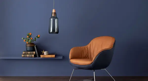 Ein Sessel mit braunem Leder und dunkelblauem Stoff vor einer blauen Wand. Orange Blumen auf einem Regal. Welche Farbe passt zu Blau? Braun!
