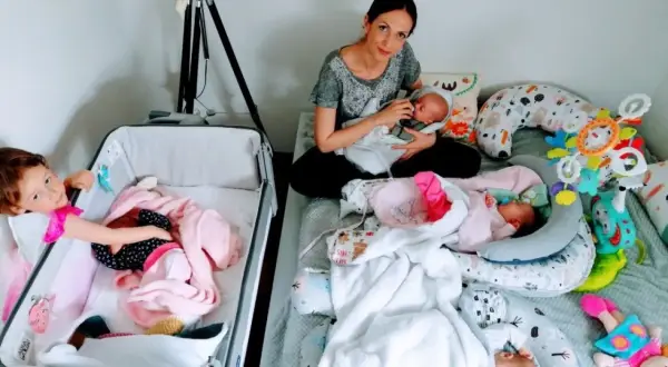 Mama karmi jedno z czworaczków, podczas gdy starsza siostra opiekuje się drugim dzieckiem w łóżeczku.