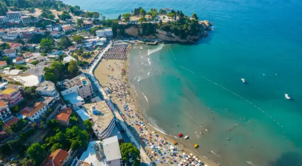 Słoneczne kotor plaże tętnią życiem. Tłumy ludzi odpoczywają pod parasolami, a w turkusowej wodzie kąpie się wielu plażowiczów.