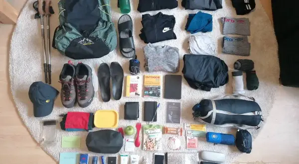 Packliste Jakobsweg: Rucksack, Wanderschuhe, Kleidung, Wasserflasche, Wanderstöcke, Reiseführer und weitere Essentials für den Pilgerweg.