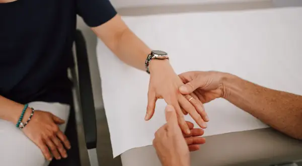 Therapeut untersucht die Hand einer Patientin, um einen Schnappfinger zu behandeln.