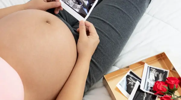 Kiedy rośnie brzuch w ciąży, przyszła mama ogląda zdjęcia USG. W pudełku z różami czekają kolejne pamiątki.