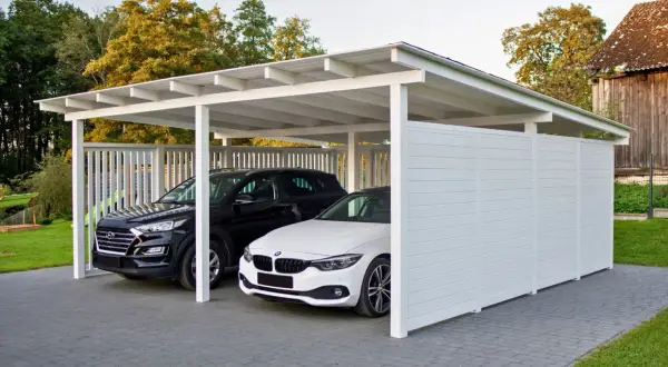 Nowoczesne wiaty garażowe chronią czarne i białe auto. Eleganckie, białe konstrukcje idealnie komponują się z otoczeniem.
