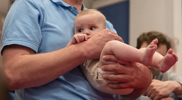 Niemowlę w ramionach mężczyzny, z odginaniem głowy do tyłu, patrzy zaciekawione.