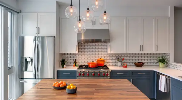 Cucina moderna con isola in legno, elettrodomestici in acciaio e pensili bianchi. Un modo per abbellire una cucina moderna è con tocchi di colore, come le pentole arancioni sul piano cottura.