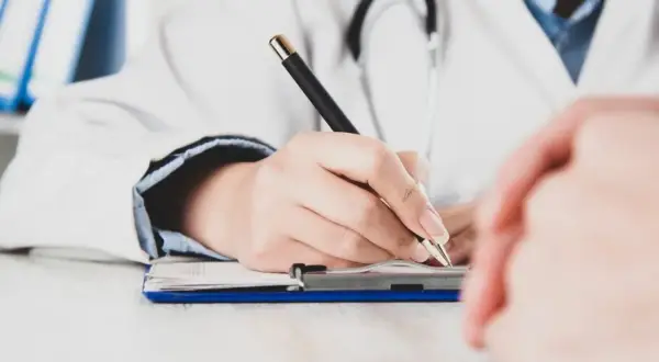 Lekarz pisze na dokumentach, zastanawiając się, czy zwolnienie od psychiatry zostaje w papierach.