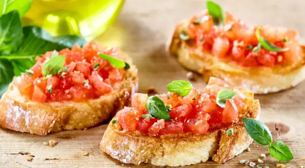 Bruschetta z pomidorami i mozzarellą, świeża bazylia i oliwa z oliwek na drewnianej desce.