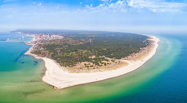 Malownicze wybrzeże pomorza gdańskiego z piaszczystą plażą, lasem sosnowym i miasteczkiem nad zatoką.